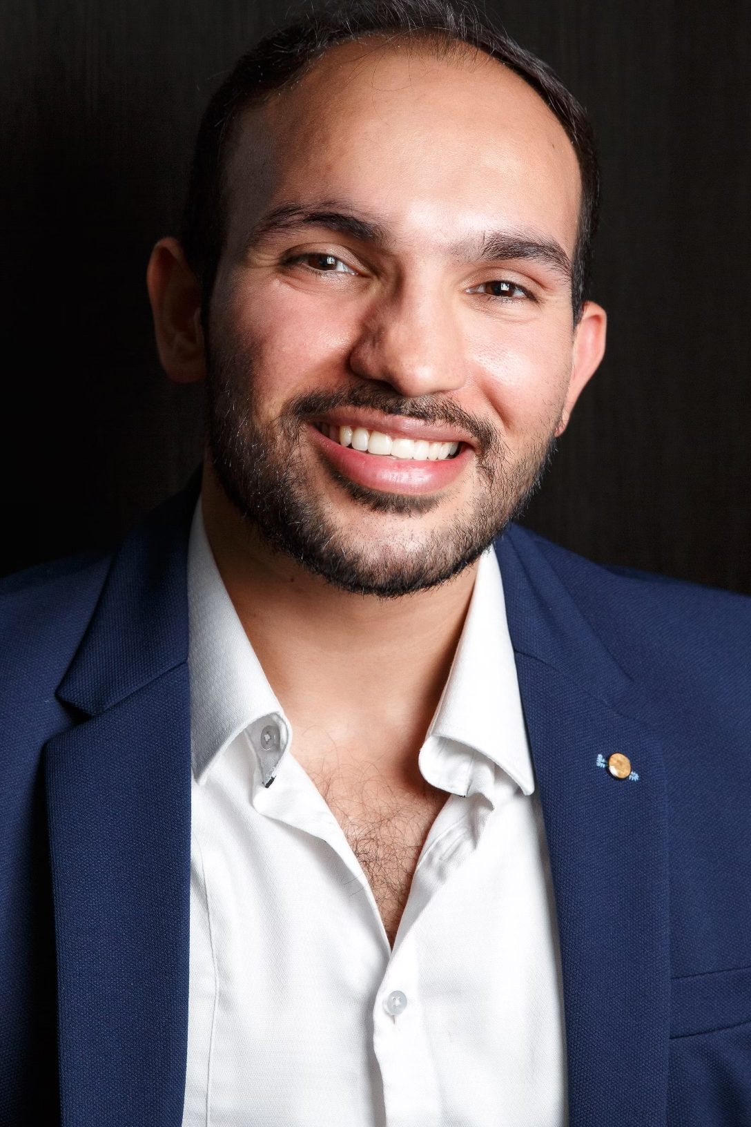 ADHD GP Dr Jaspreet Saini in a navy blue blazer and white shirt, posing against a dark background.